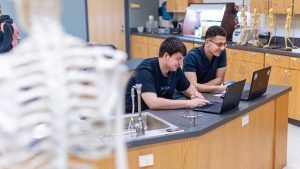 Two male students work at laptops in a biology lab