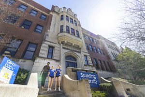 three students talking and walking out of a tall campus building