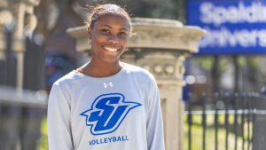 A black female student in a Spalding volleyball long sleeve shirt smiles directly at the camera in a portrait shot