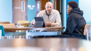 student and teacher talking at a table in front of device
