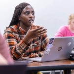 female student speaking in class with laptop open on desk in front