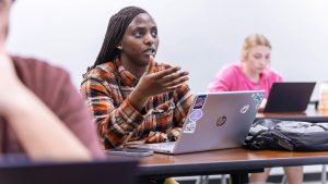 female student speaking in class with laptop open on desk in front