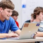 male student smiling while looking at laptop during class