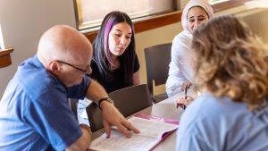 male teacher sitting with three students looking at a book