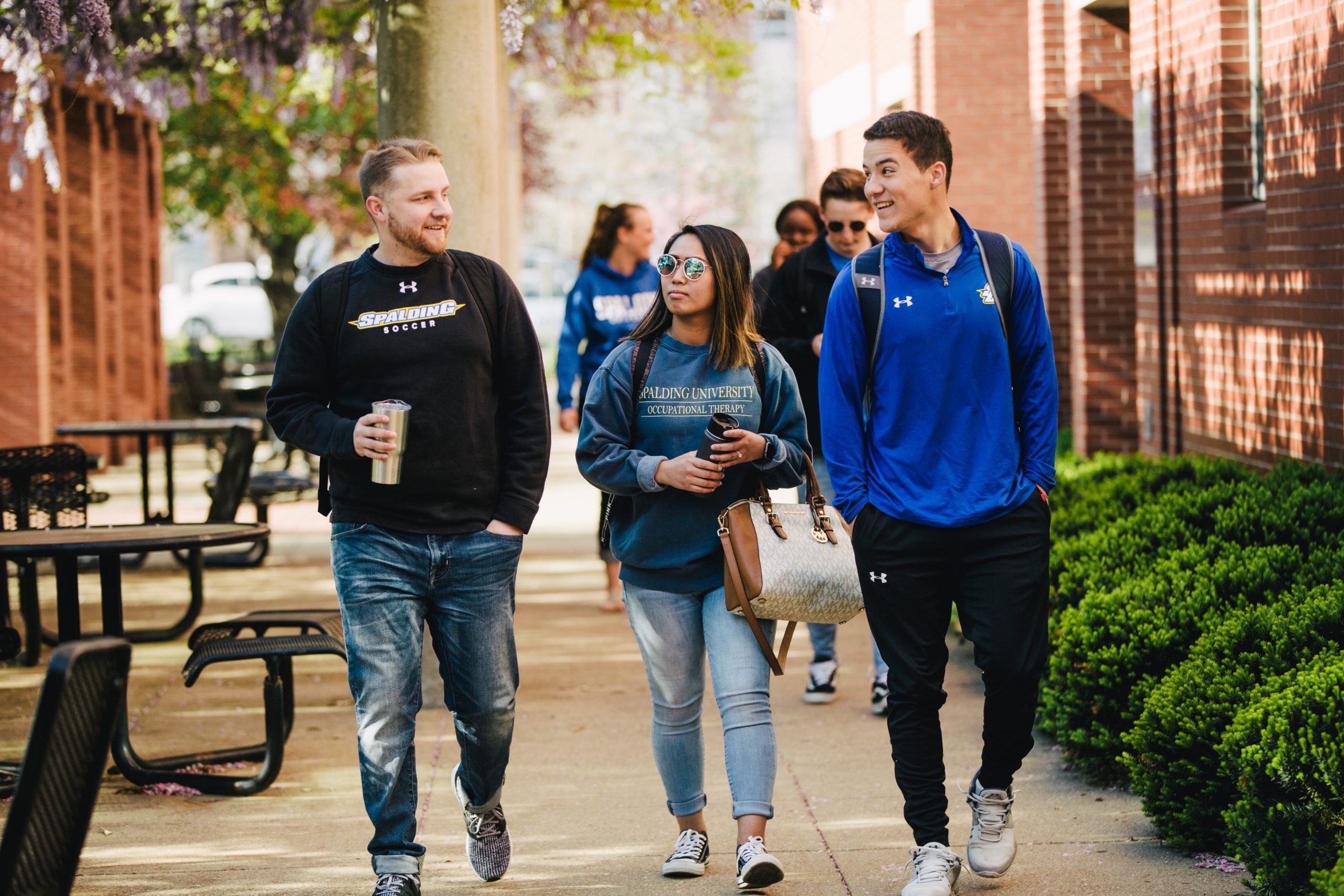Group of three students wearing Spalding gear walk together on a sidewalk