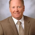 Headshot of Larry Owens, white male in beige suit and tie