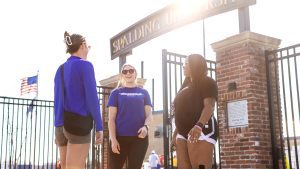 Three Spalding female students in athletic wear stand outside the stadium entrance