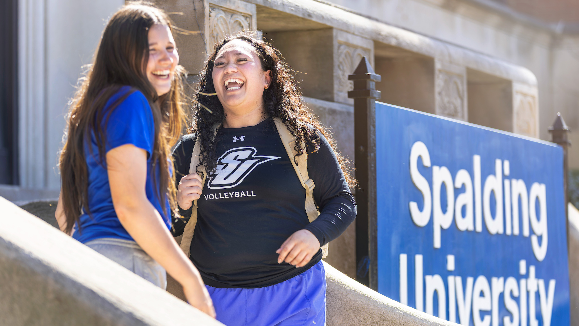 Two female Spalding university students stand outdoors laughing together