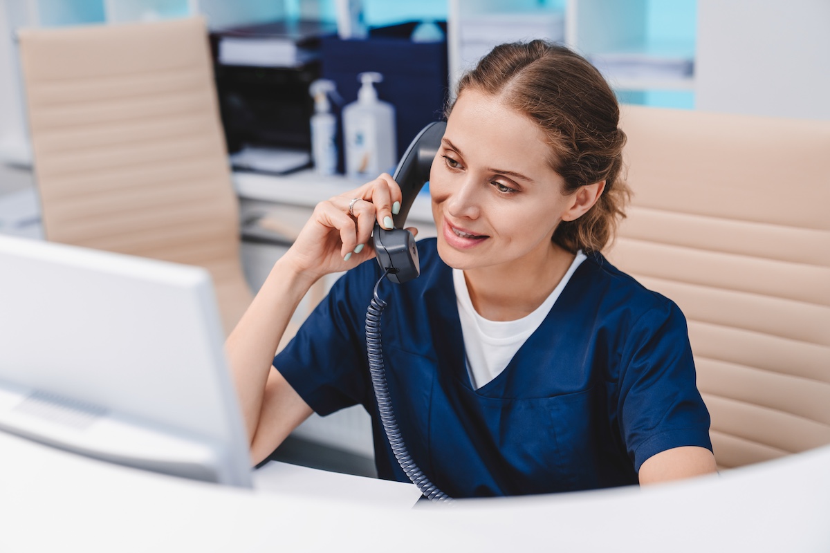 Medical assistant talking on phone in clinic while sitting at computer