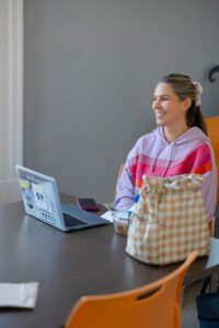 Female student in pink sweatshirt sits at a table with a laptop