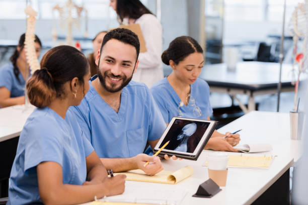 Three students in light blue scrubs review x-ray images on a tablet sitting in a classroom