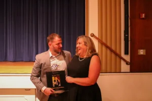 male and female standing with award in front of stage